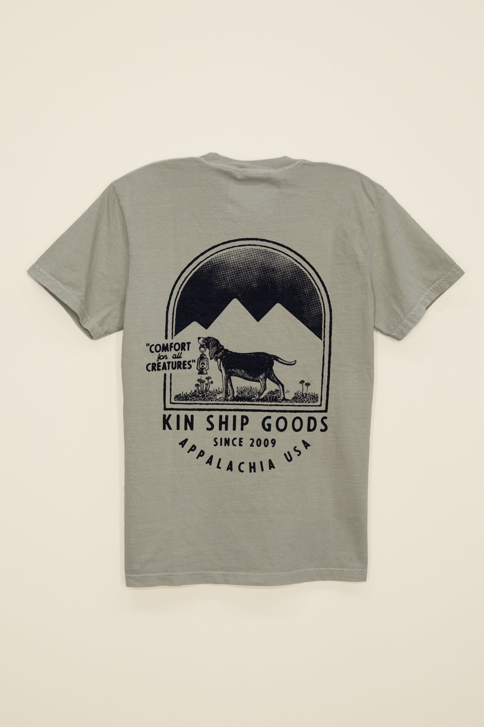 Kin Ship Goods beagle pocket tee in sage with mountain scene and ‘Comfort for all Creatures’ graphic on back.