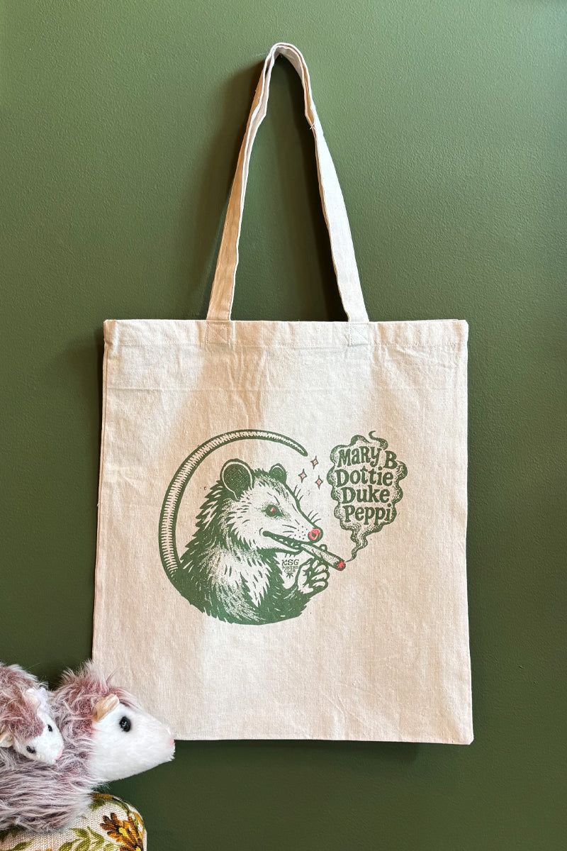 Kin Ship Goods tote bag with green opossum smoking illustration and “Mary B, Dottie, Duke, Peppi” biscuit names in a speech bubble.