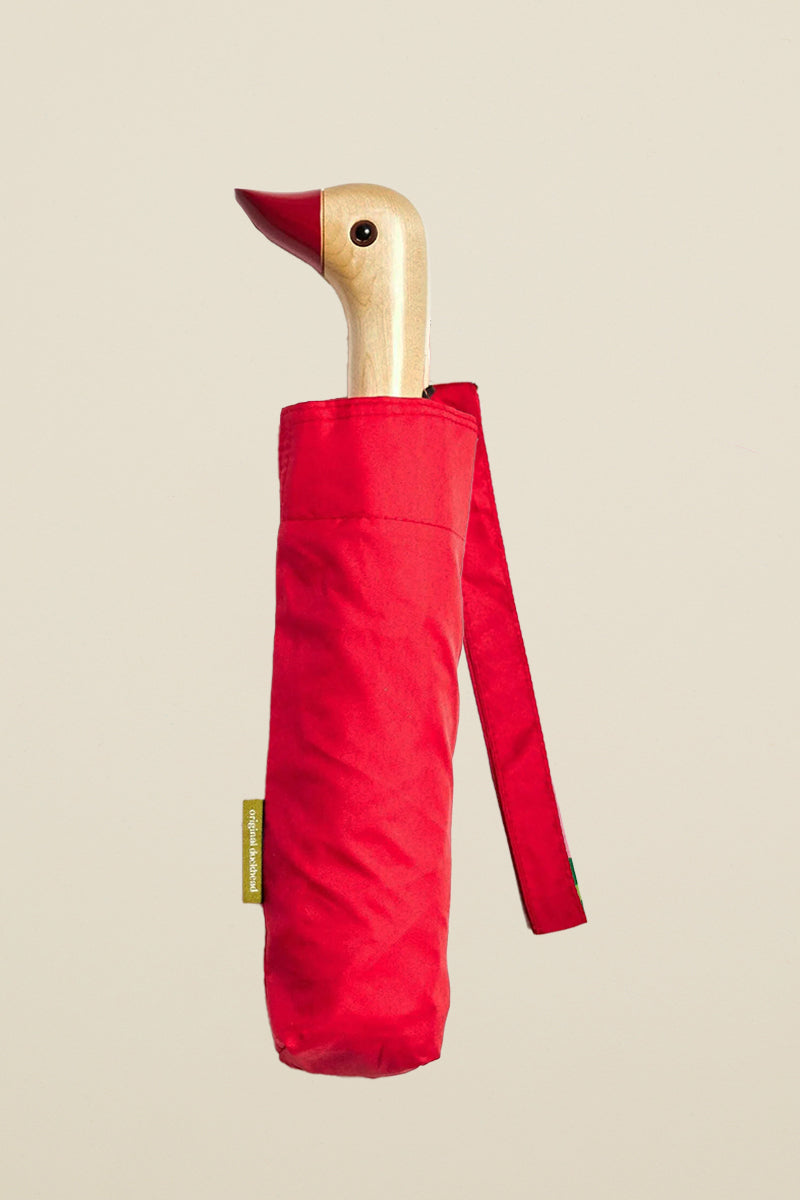 Kin Ship Goods compact red umbrella with wooden duck head handle and red beak—fun and functional rainy day accessory with personality.